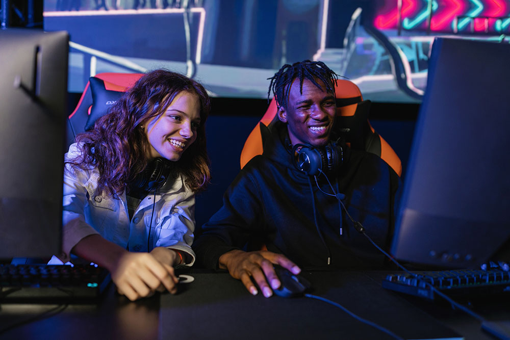 Guy and girl sitting at gaming PCs and smiling at video game event.