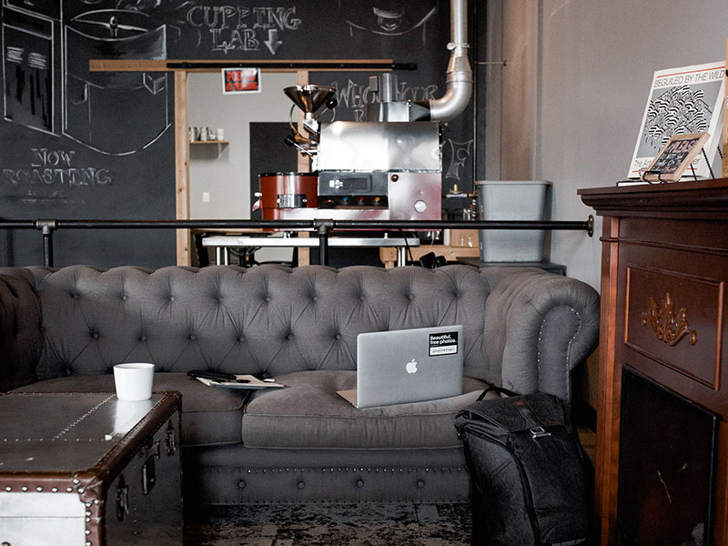 Coffeehouse with gray couch and trunk table with laptop and coffee mug on table.